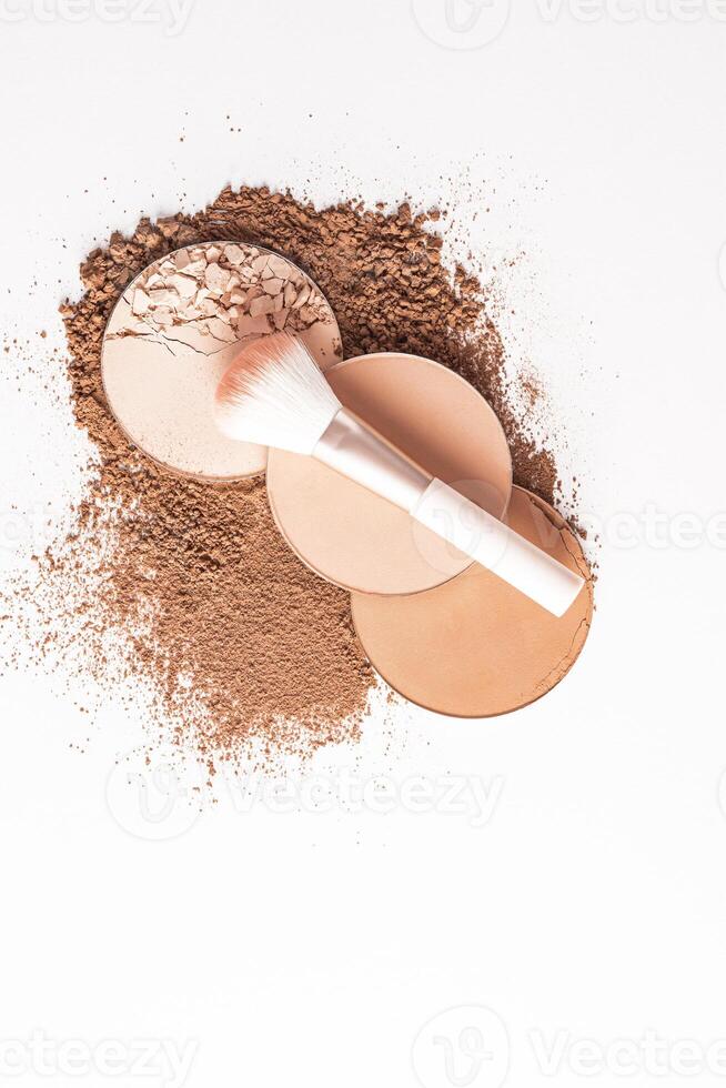 Three round blocks of compact powder in different tones, a makeup brush lies on them. top view. white background. a layout product. vertical top view. photo