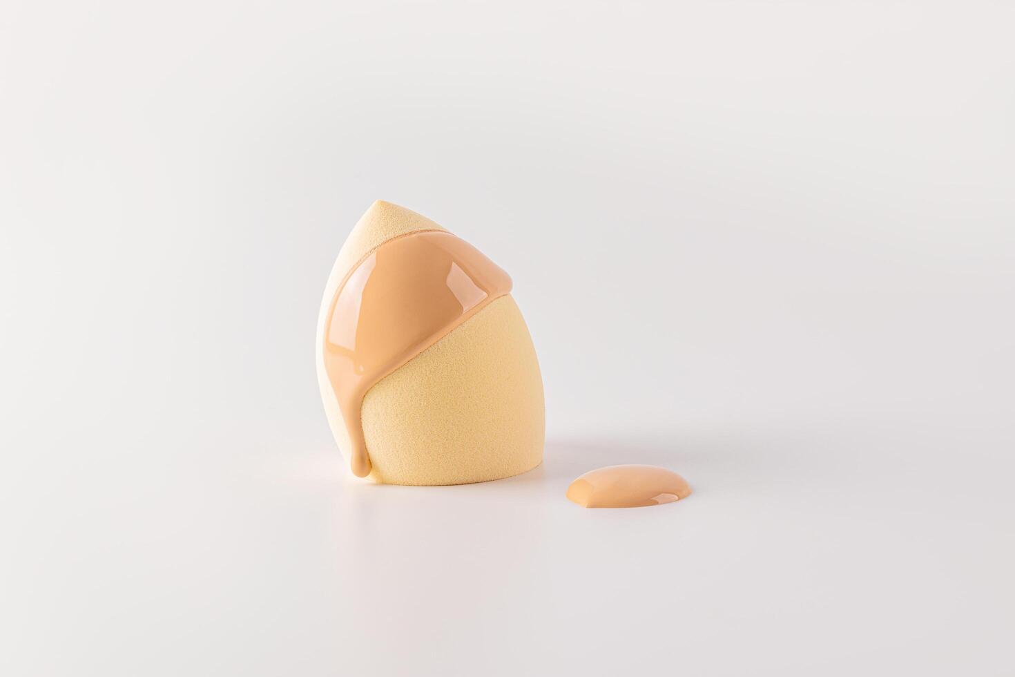 Liquid foundation powder on a beige cosmetic sponge blender in the shape of an egg. The concept of applying makeup face. Front view. white background. photo