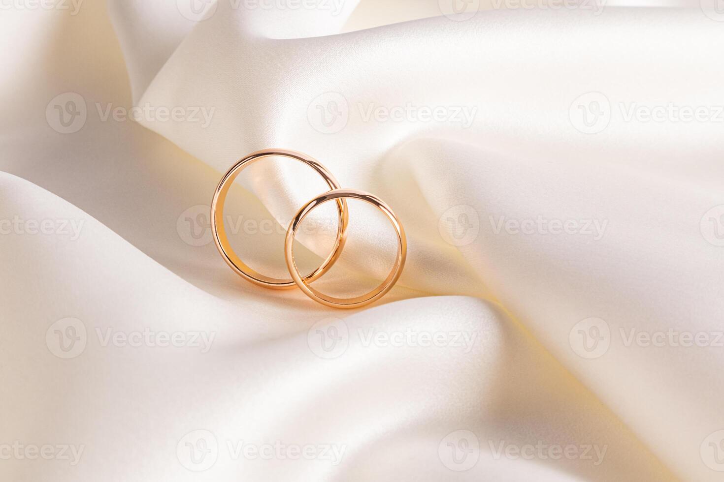 Two gold elegant wedding rings lie on soft folds of beige satin fabric. stylish wedding background. postcard. invitation. Product presentation. photo