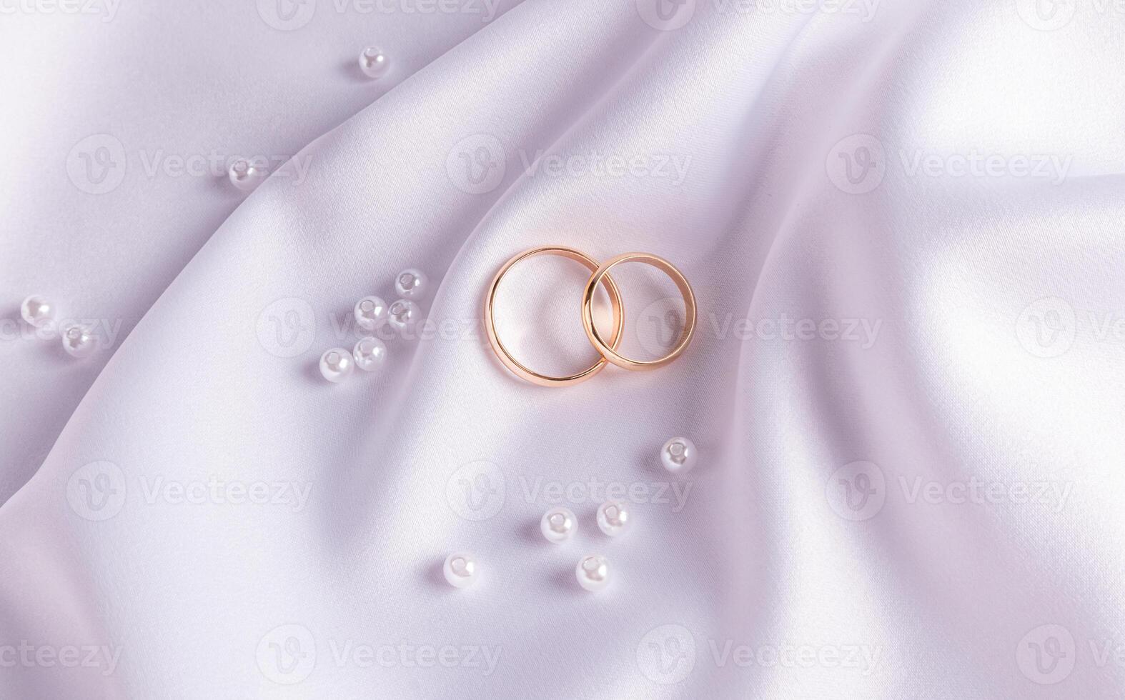 Chic wedding background with wedding gold rings lying on a wave of white satin fabric and pearls. The concept of the wedding. postcard. top view. photo