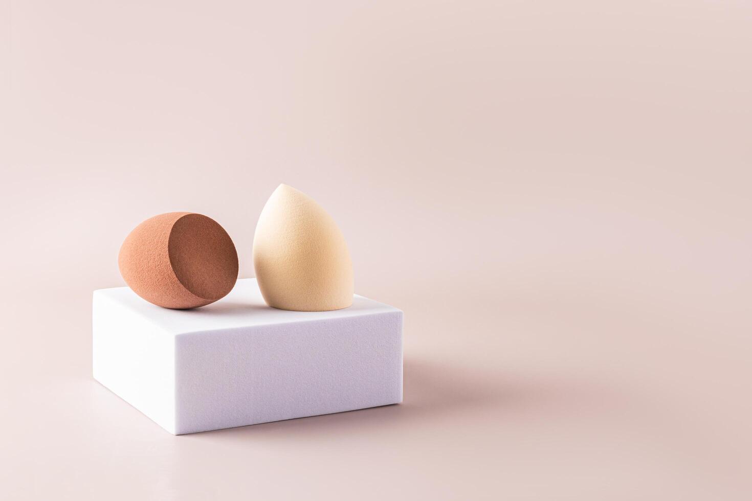 Beige and brown egg-shaped beauty sponge blenders on a square white catwalk and beige background. Front view. A sample of a makeup tool. A copy space. photo