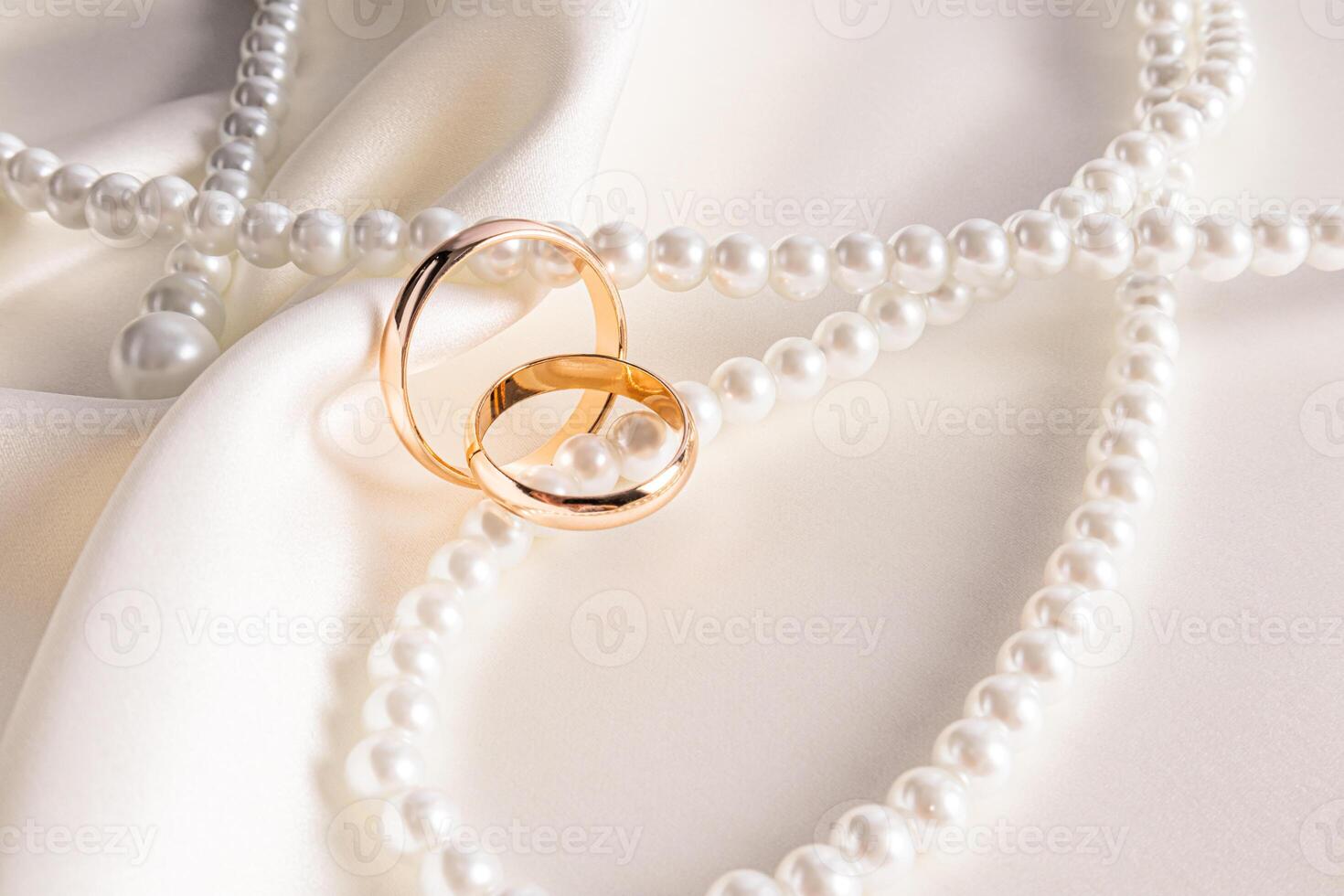 pair of gold wedding rings lying on a chic string of pearl beads on beige satin. Template postcards, invitations. wedding background. front view. photo