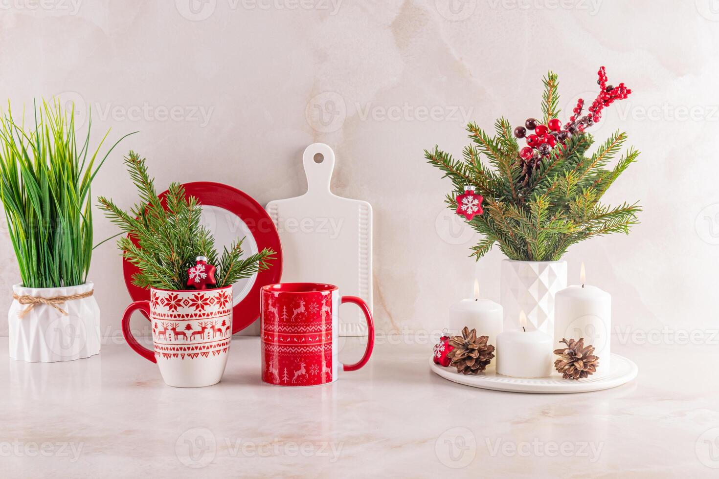 Christmas bright mugs with ornaments, spruce branches, cones, decorations on the kitchen marble countertop in a modern kitchen interior. Front view. photo