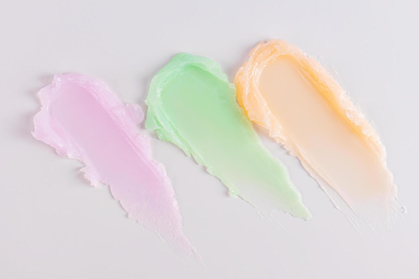 Three multicolored smeared lip balm samples on a white background. Cosmetic texture sample. delicate pastel texture colors. Layout for presentation. photo