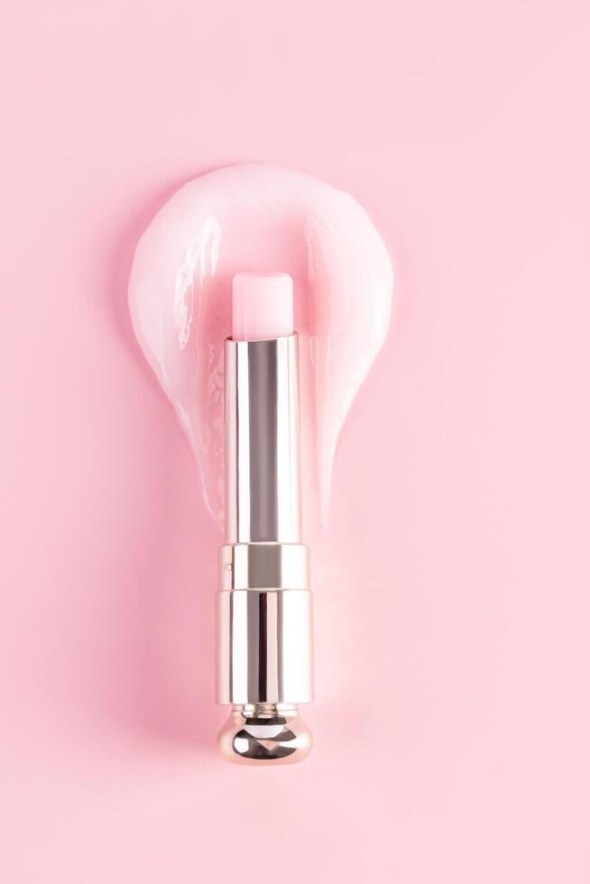 An open package of a tube of lip balm with a delicate structure to moisturize and nourish the lips lies on a sample of rose balm. vertical top view photo