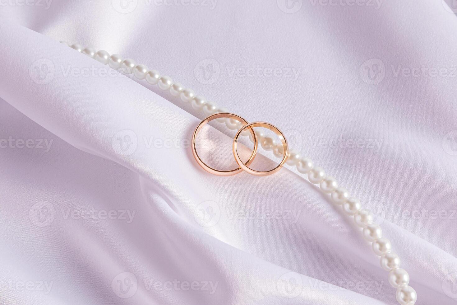 Beautiful wedding arrangement with two gold wedding rings white satin fabric, pearl beads. wedding card, invitation. space for text photo