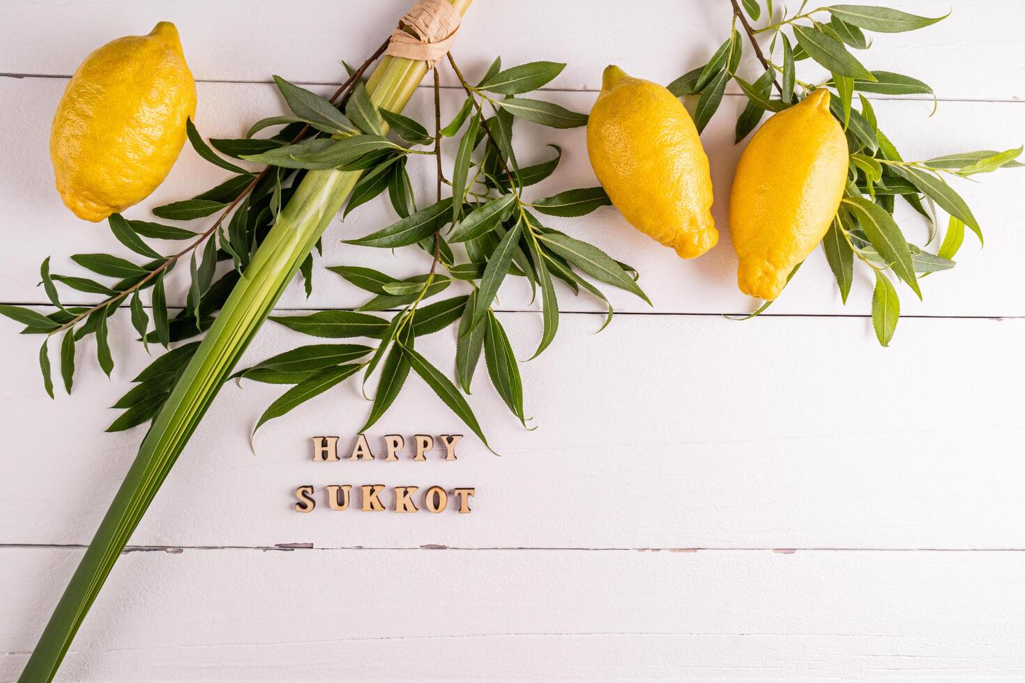 tied palm branches, willow branches, citrus fruits in a wicker basket on white wooden boards and a towel in blue white. Wooden letters of the Sukkot photo