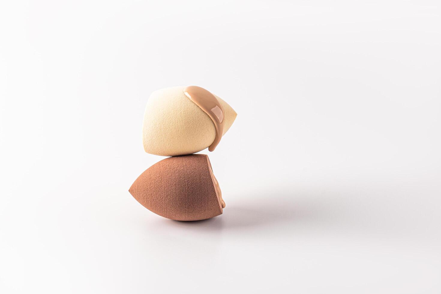 The delicate liquid texture of foundation powder in a natural tone flows down on a blender sponge. Two sponges of different colors. white background. photo