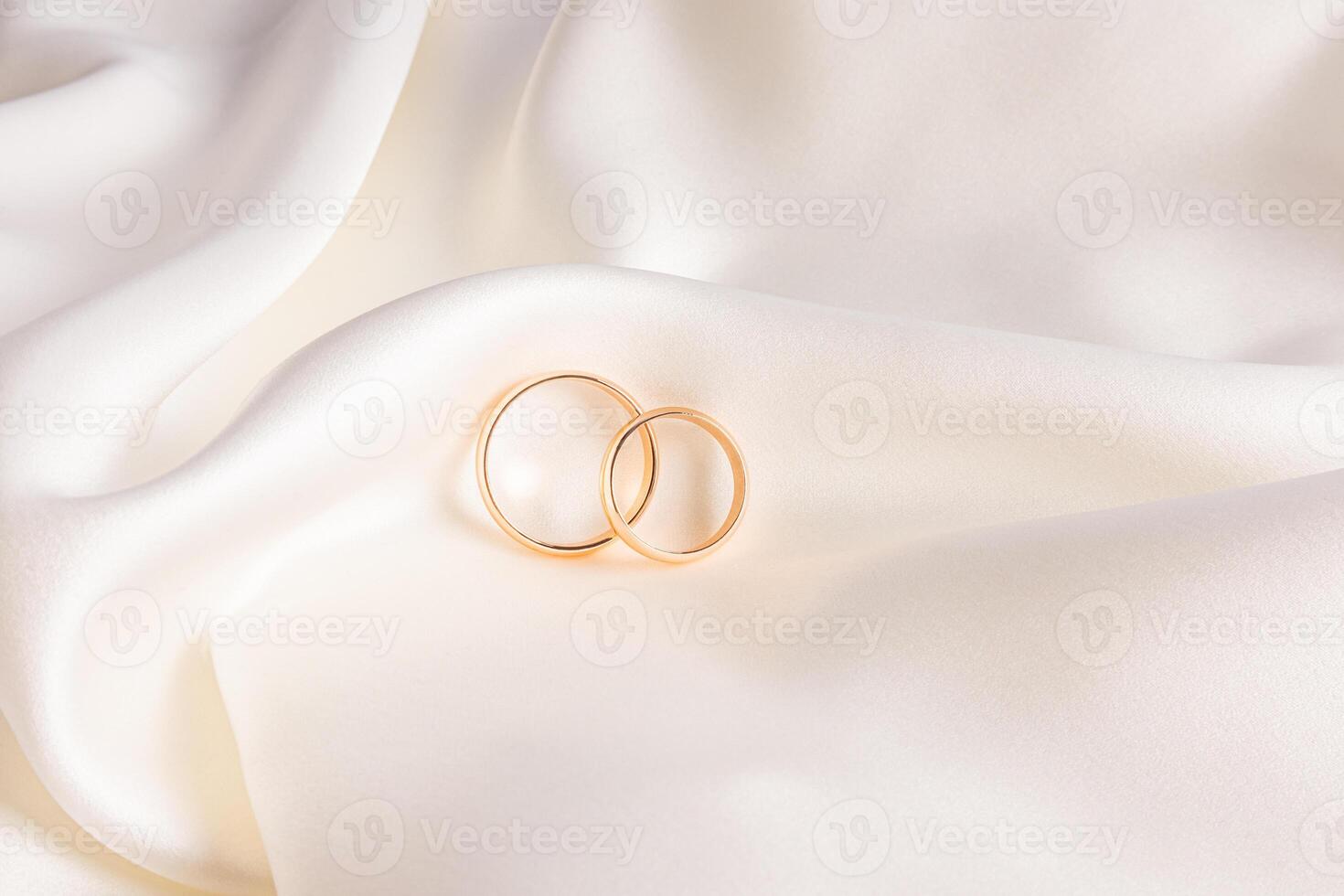 Two gold elegant wedding rings lie on soft folds of beige satin fabric. stylish wedding background. postcard. invitation. Product presentation. photo