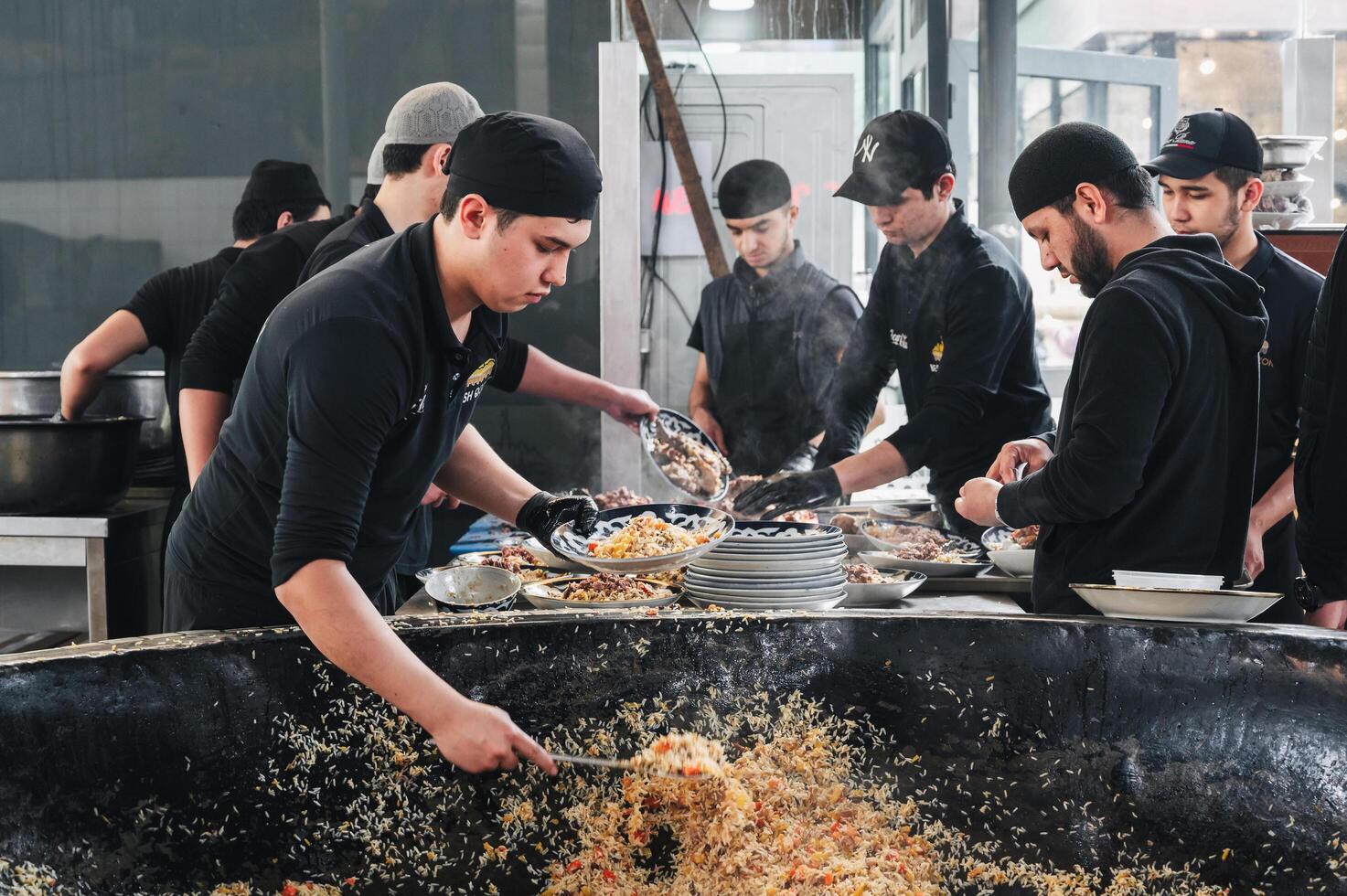 male cooks put ready-made traditional Uzbek pilaf from big cauldron on plates in Central Asian Pilaf Center Besh Qozon. Tashkent, Uzbekistan - April 16, 2024 photo