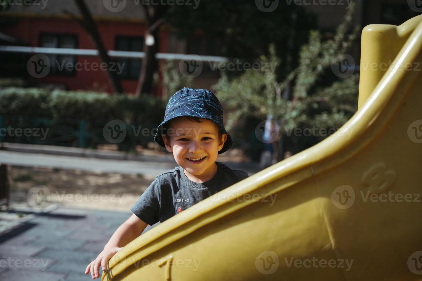happy kindergarten boy rides a slide on playground in summer photo