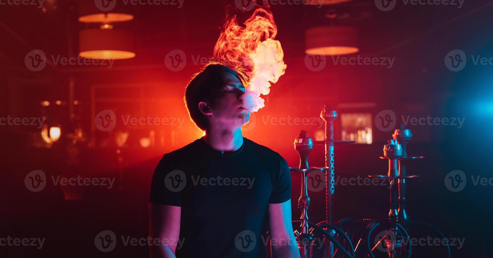 young guy smokes a shisha and lets out a cloud of smoke photo