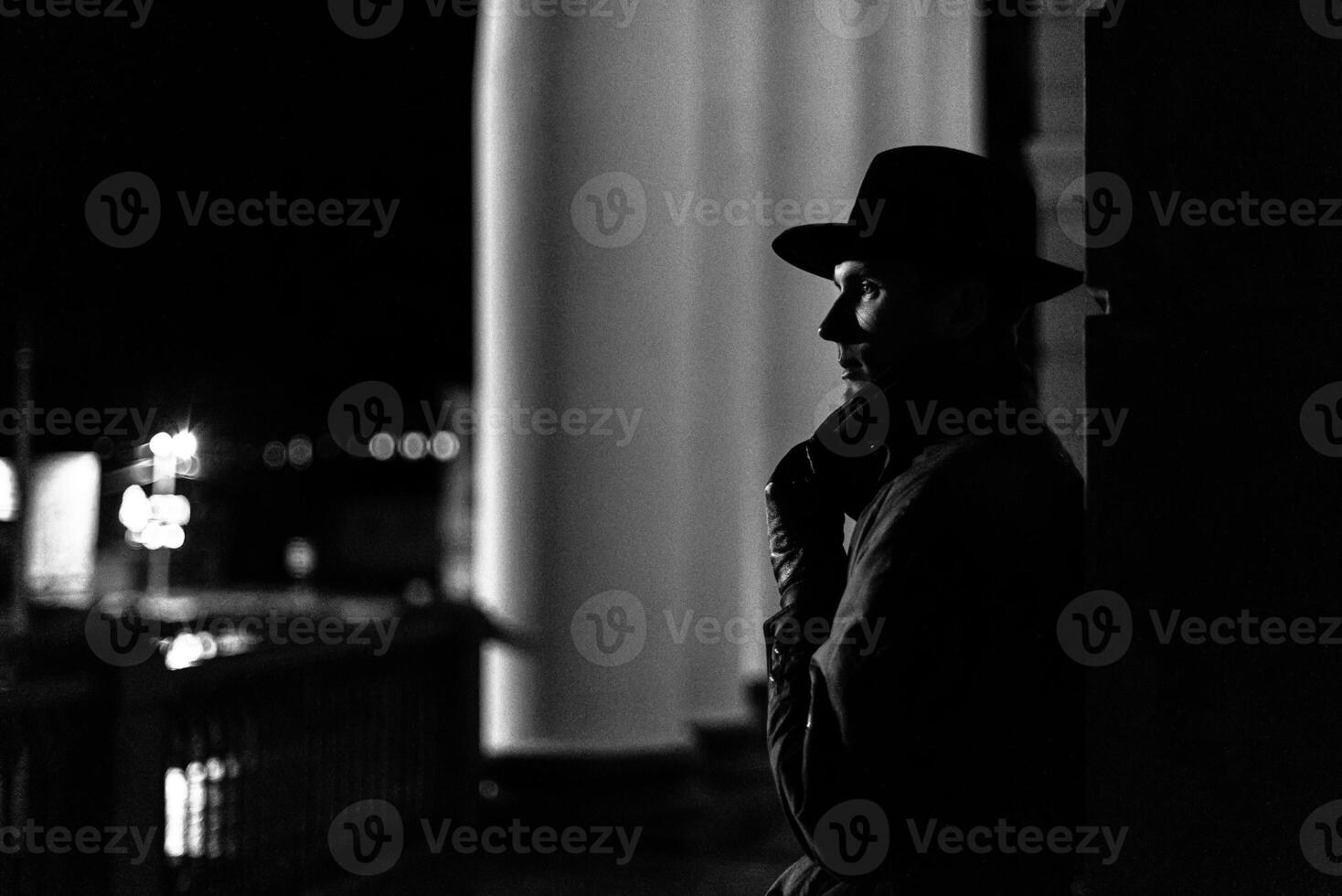 dark silhouette of a man in a raincoat with a hat and a scar on his face at night photo