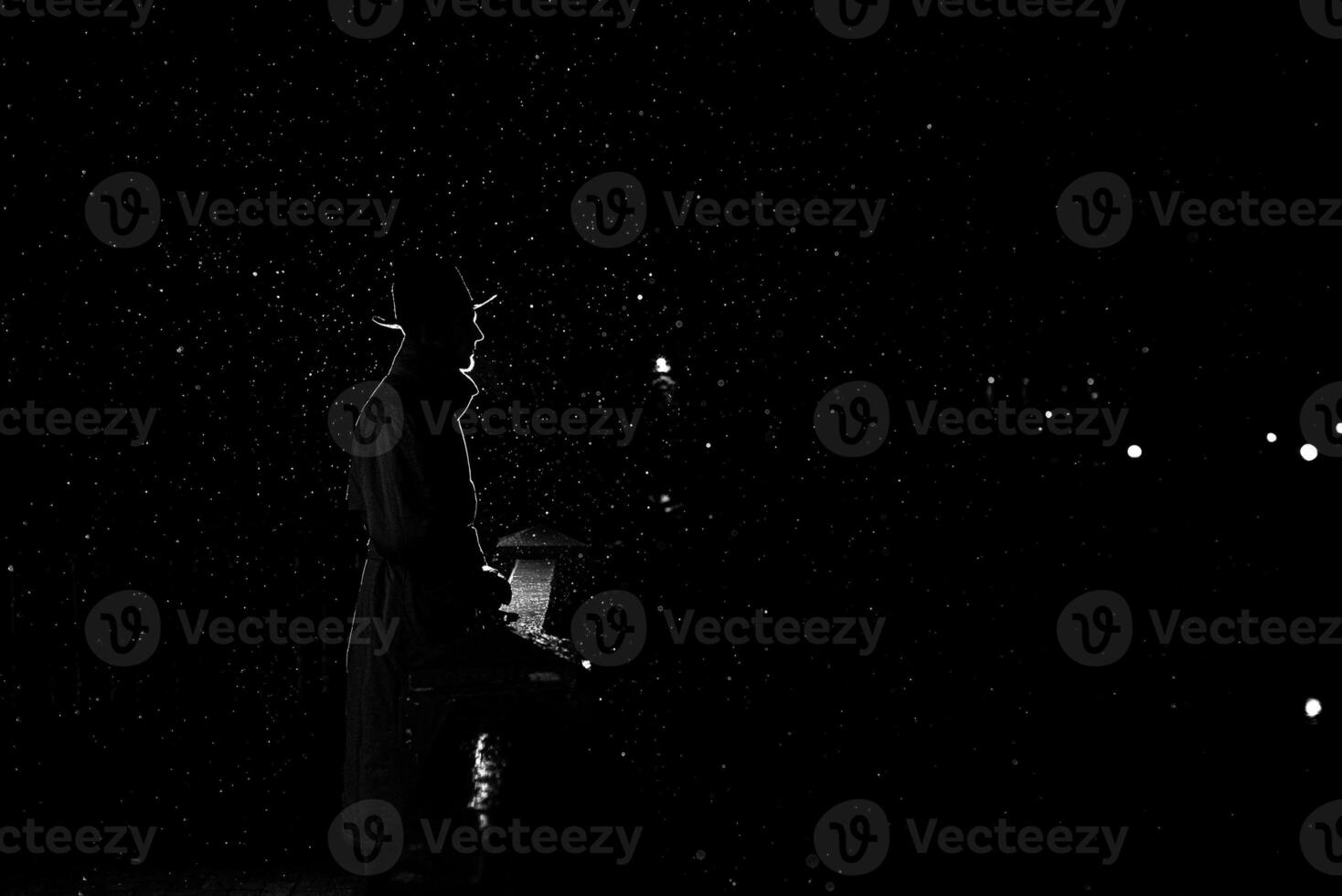 dark silhouette of a man in a hat at night in the rain in the city photo