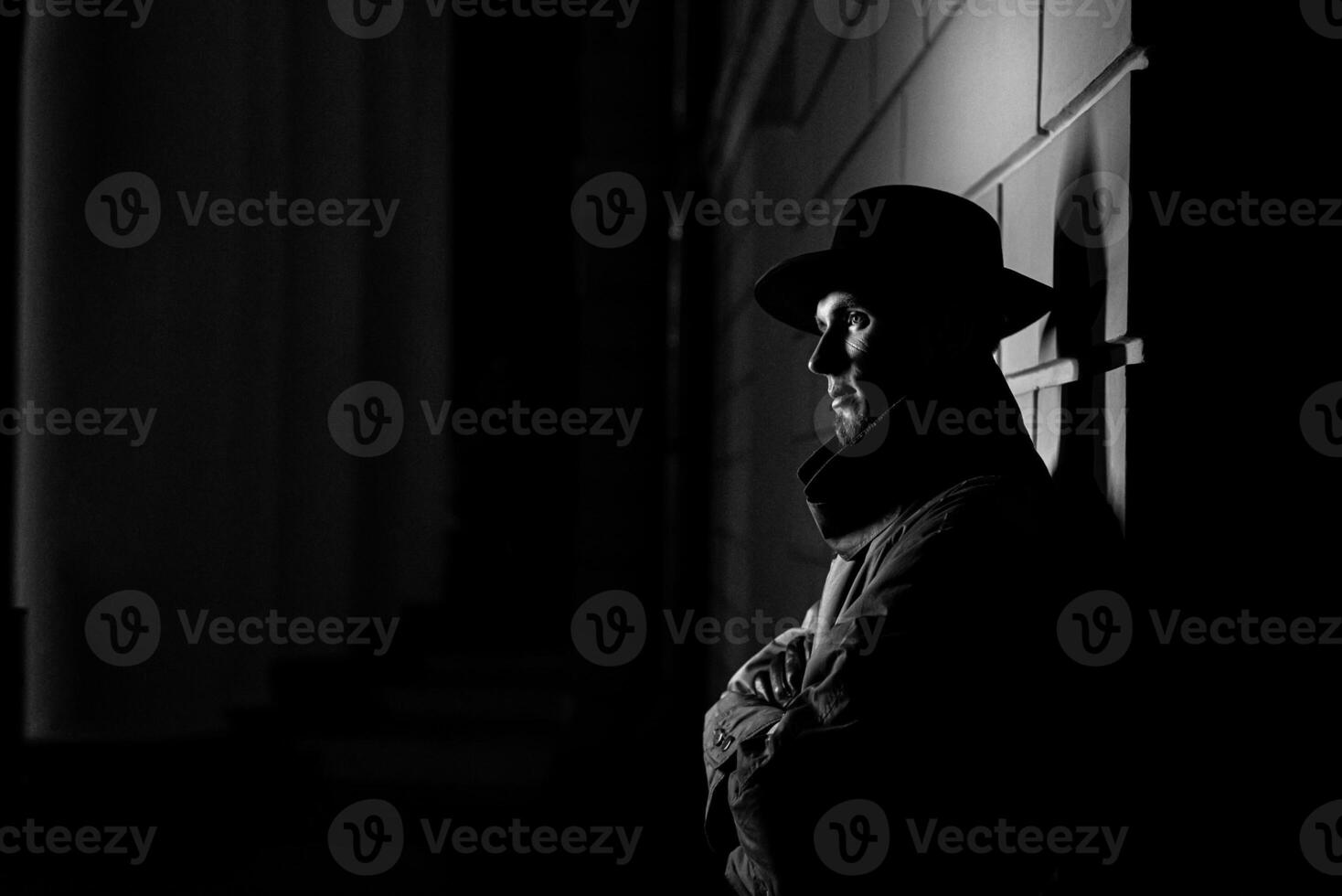 dark silhouette of a man in a raincoat with a hat and a scar on his face at night photo