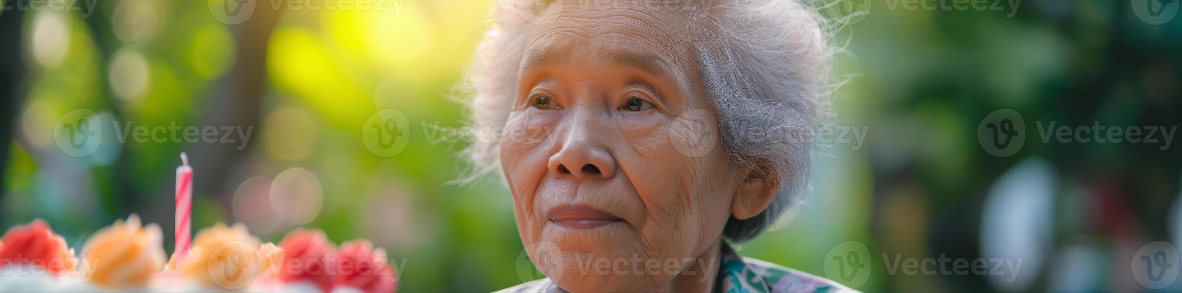 Elderly Woman Celebrating Birthday Outdoors with Candlelit Cake in Sunlit Garden photo