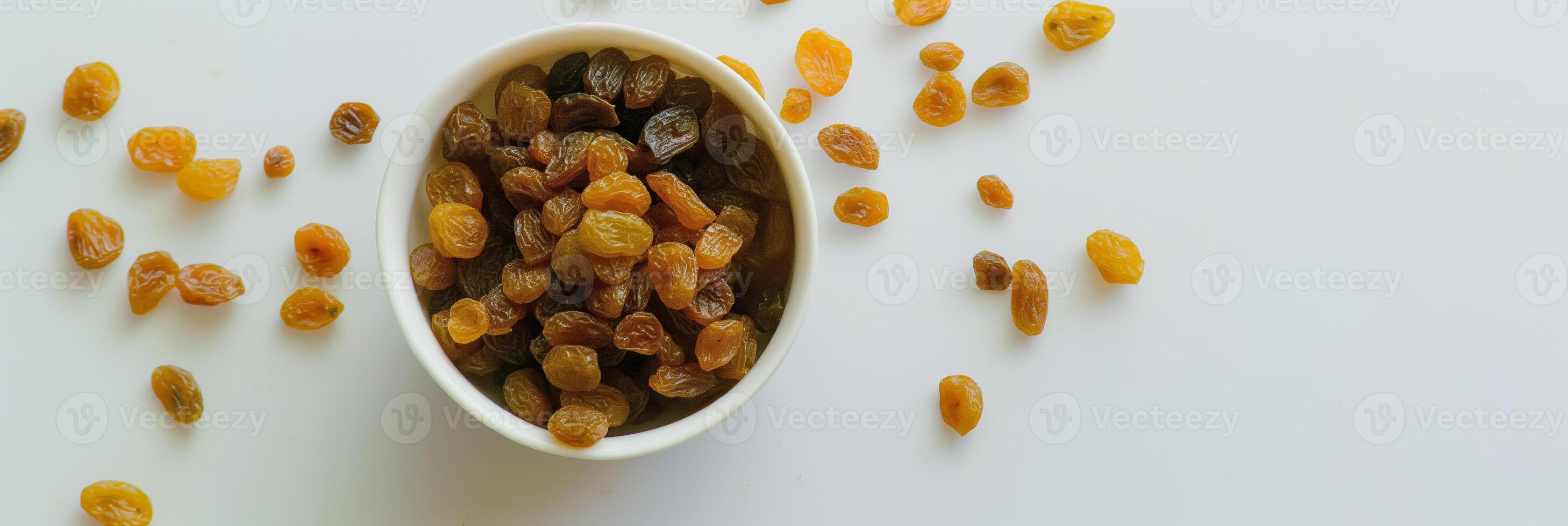 Closeup of Dried Raisins in White Bowl with Scattered Raisins on White Background photo