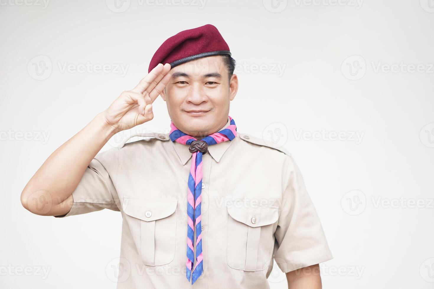 Handsome Asian man wear boy scout uniform, red cap, blue and pink striped scarf, make hand sign symbol, isolated on white background. Concept, educational career with uniform in school, Thailand. photo