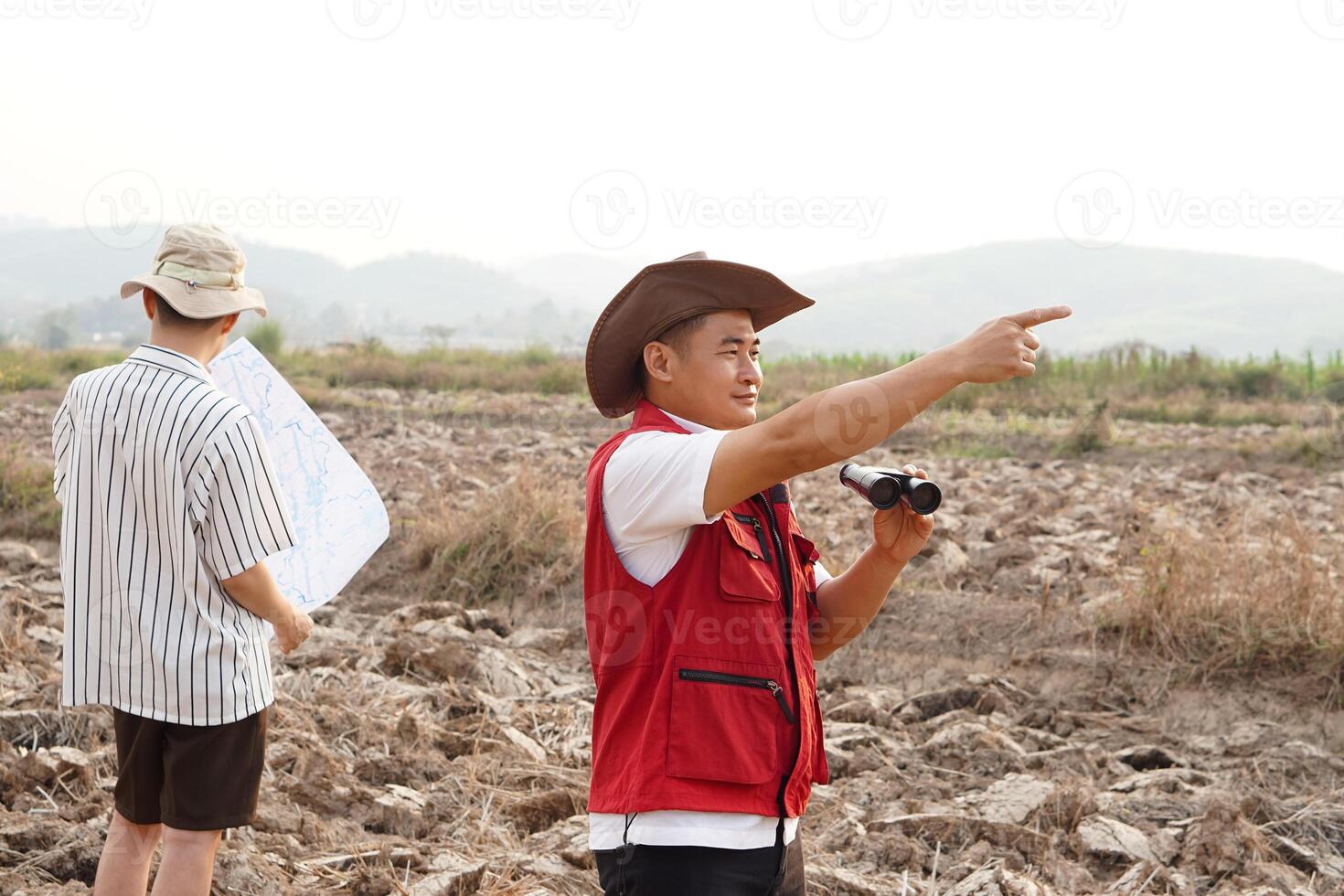 Asian father and son are exploring and surveying their own land, father holds binocular and points to boundary, son holds map. Concept, land property, legacy.Exploration. photo