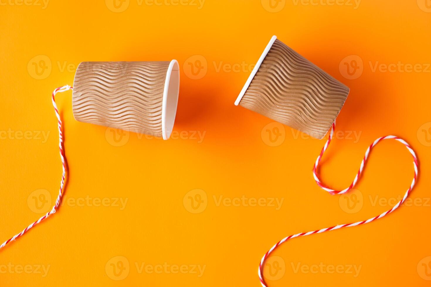 Two paper cups tied with rope for making telephone toy. Orange background. Concept, telephone toys which apply with science knowledge about vibration sound through straining strings causing us to hear photo