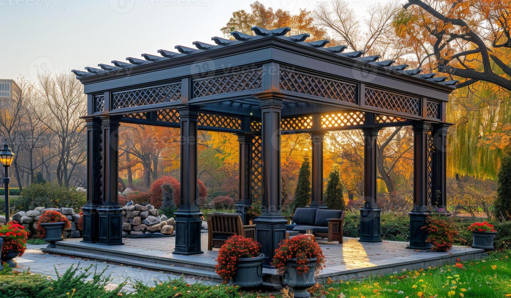 A large black gazebo with a lattice roof and a bench inside. The gazebo is surrounded by potted plants and has a few chairs and a couch inside photo