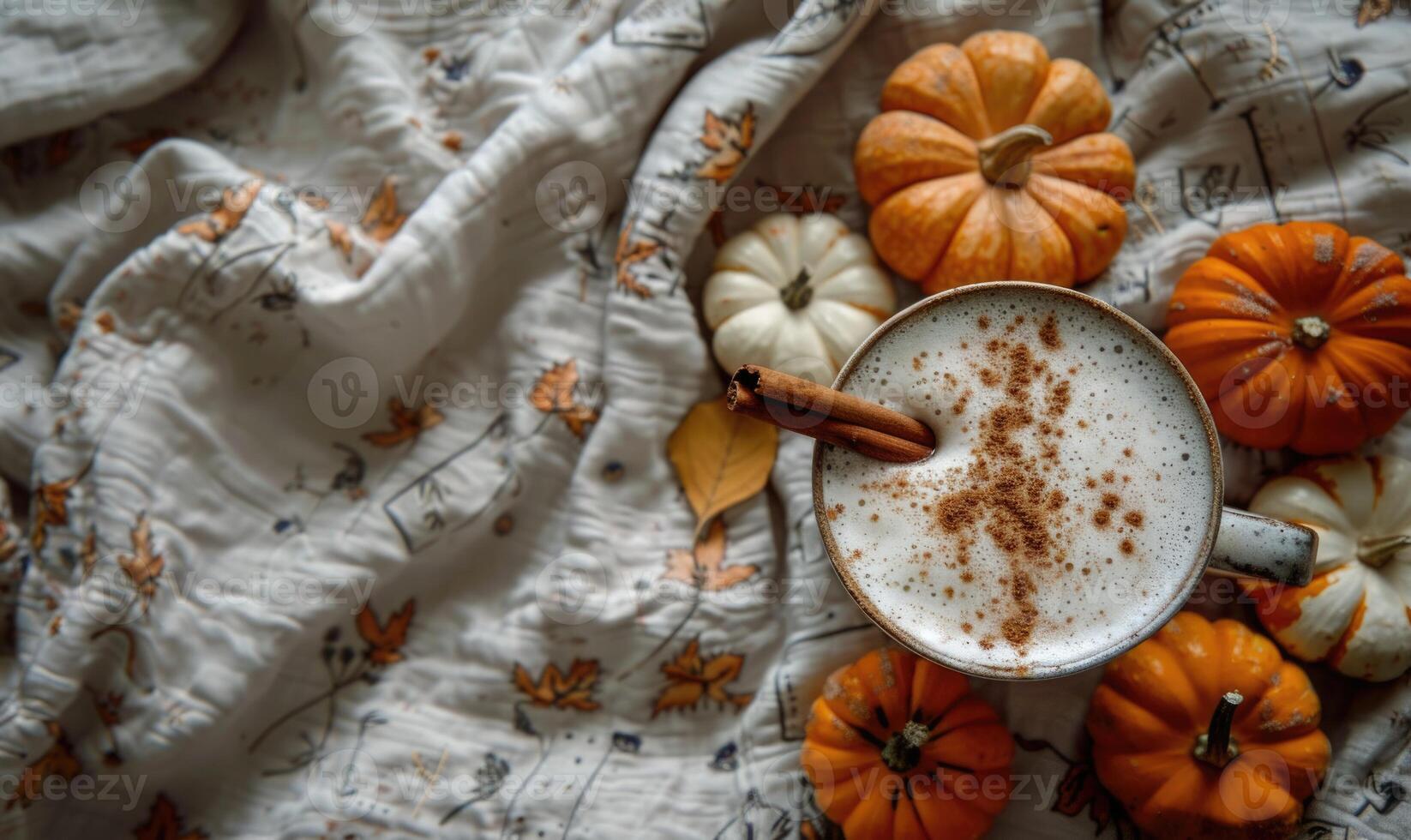 A pumpkin spice latte with a cinnamon stick, small pumpkins on a vintage tablecloth photo