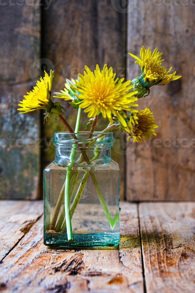 Small bouquet of dandelions in a glass vase on a wooden background. Minimalism. photo