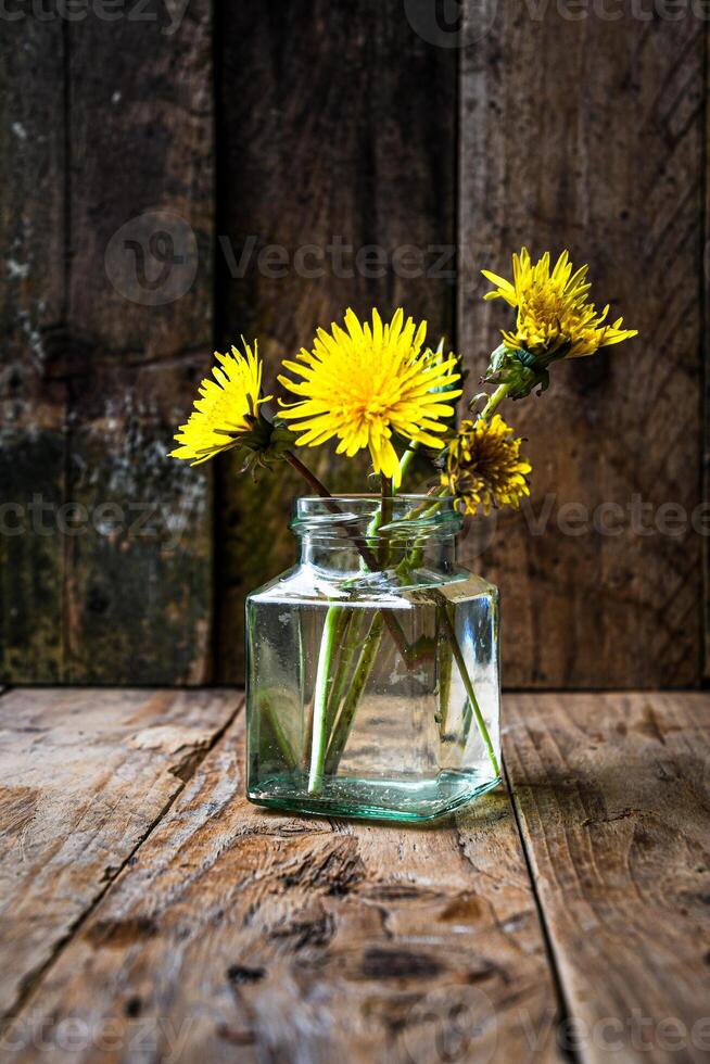Small bouquet of dandelions in a glass vase on a wooden background. Minimalism. photo