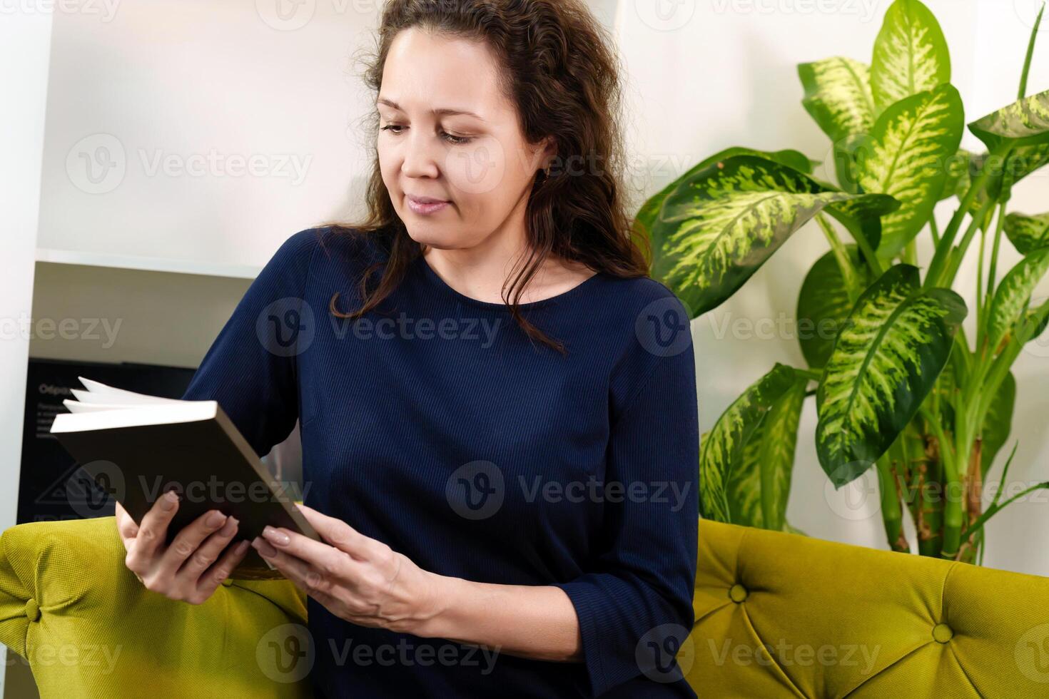 Smart and confident middle aged woman enjoying reading a book while sitting on a comfortable sofa in a modern office photo