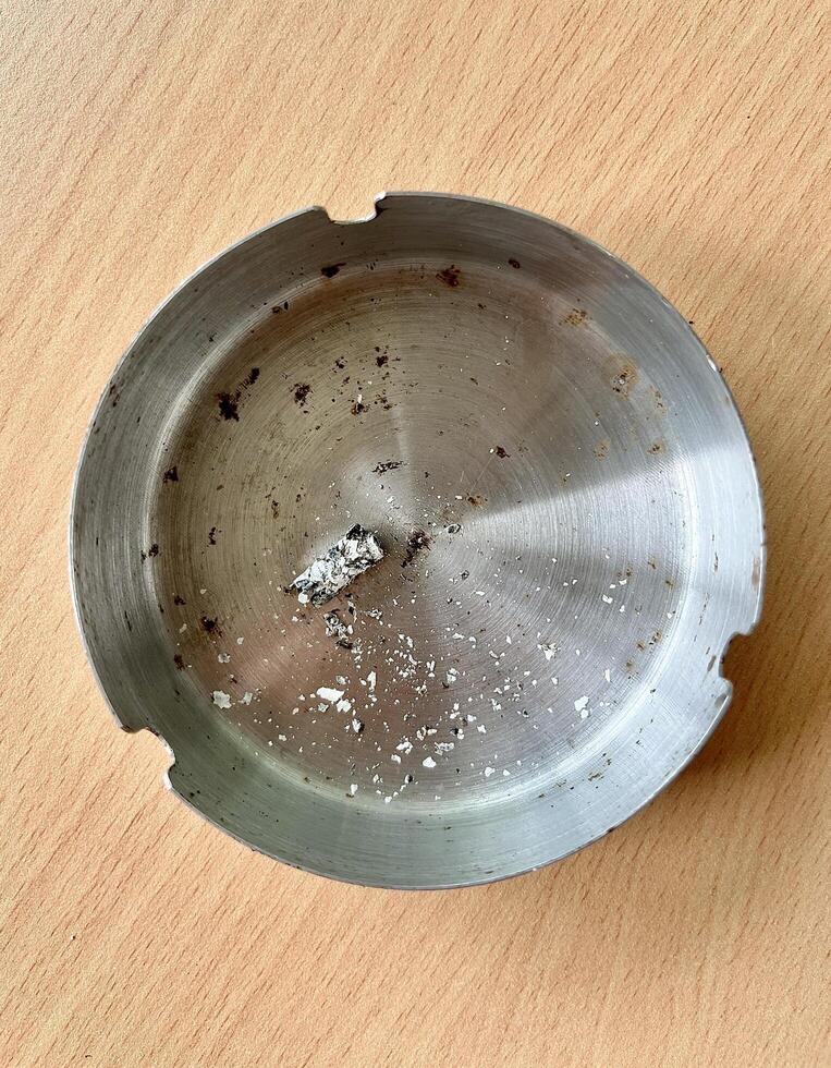 Round metal aluminium ash tray with cigarette ashes from above top angle view isolated on vertical wooden surface background. photo