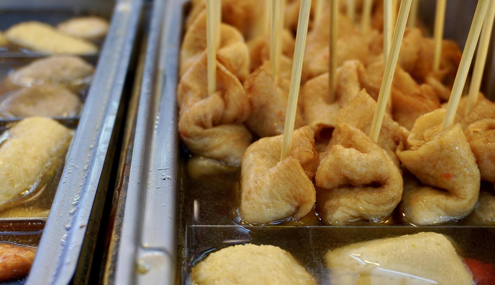 Street food fish cakes and skewers snack in hot warm soup isolated on horizontal restaurant container background. photo