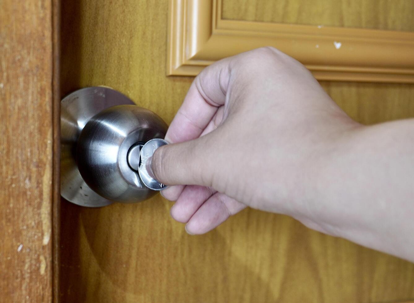 Hand holding emergency coin key to unlock round cylinder metal bathroom door knob isolated on horizontal background. photo
