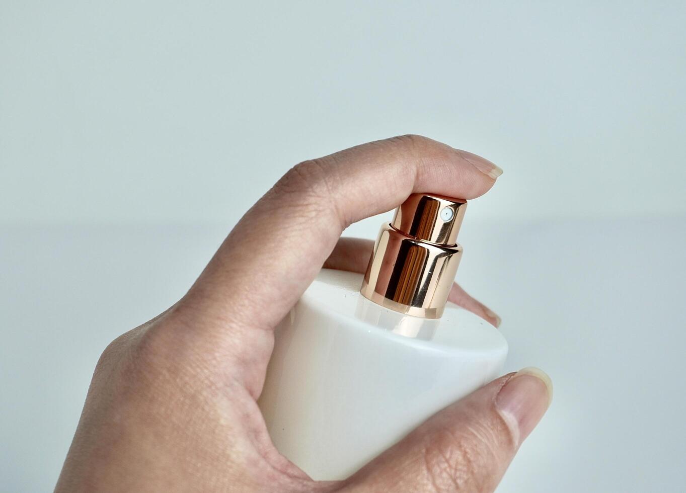 Human hand with holding and pressing gesture on perfume bottle spray object isolated on horizontal white background. photo
