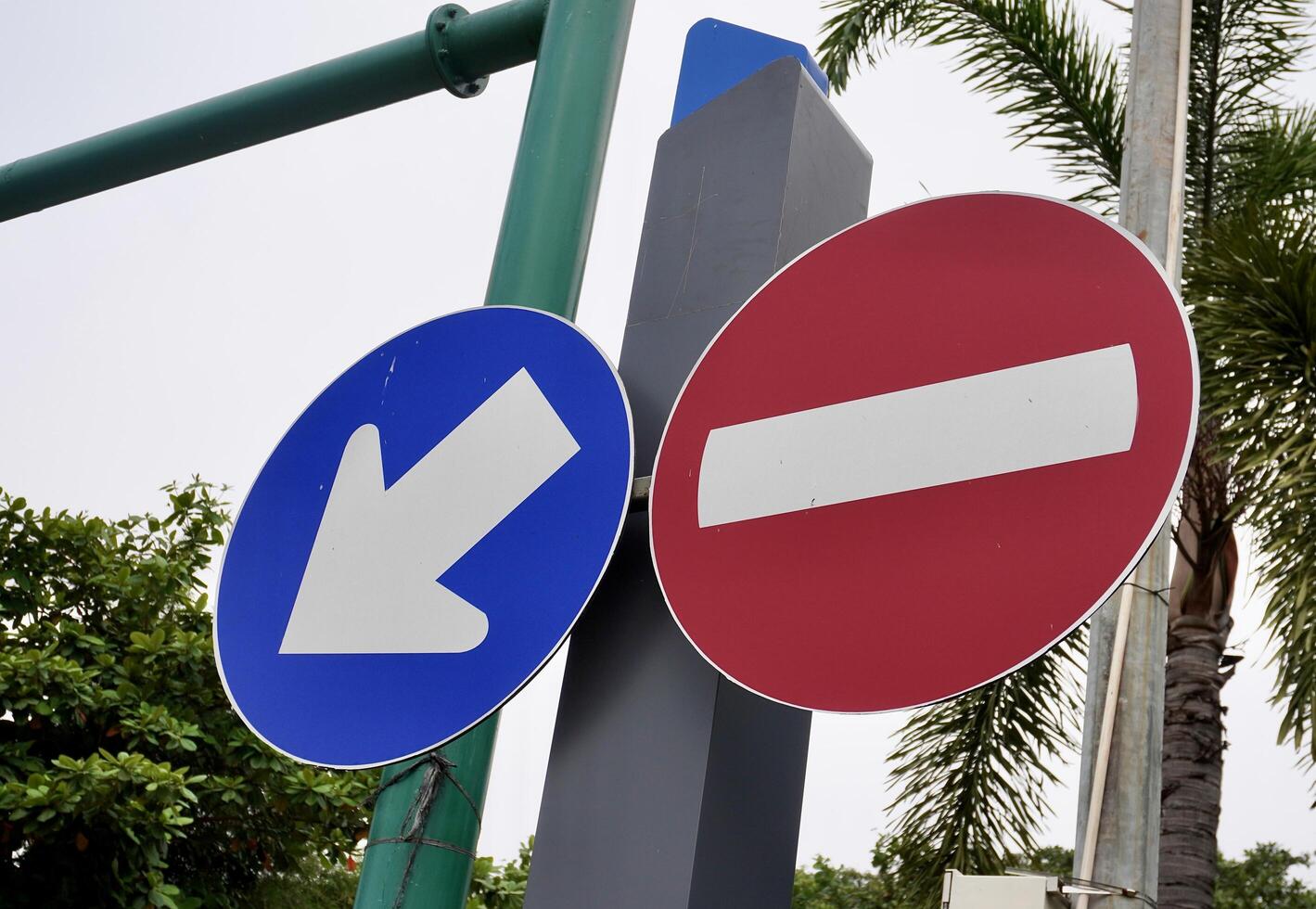 Blue white arrow and red white do not enter round shaped road sign isolated on horizontal outdoor sky and tree leaves background. photo