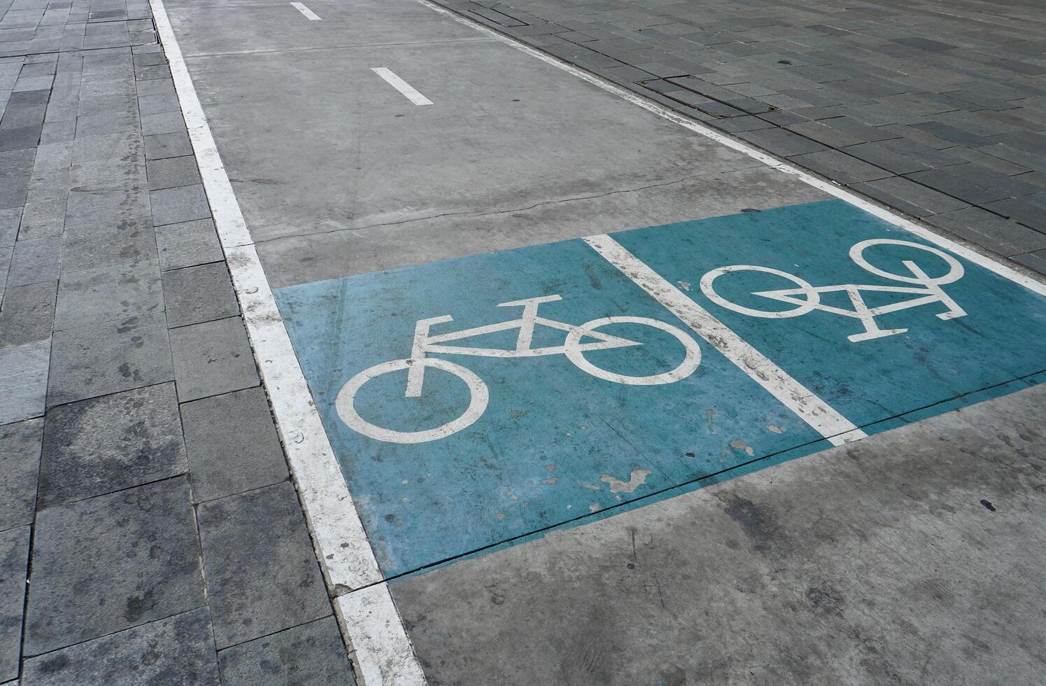 Bicycle lane white colored icon and blue paint on concrete road isolated on horizontal grey colored street background. photo