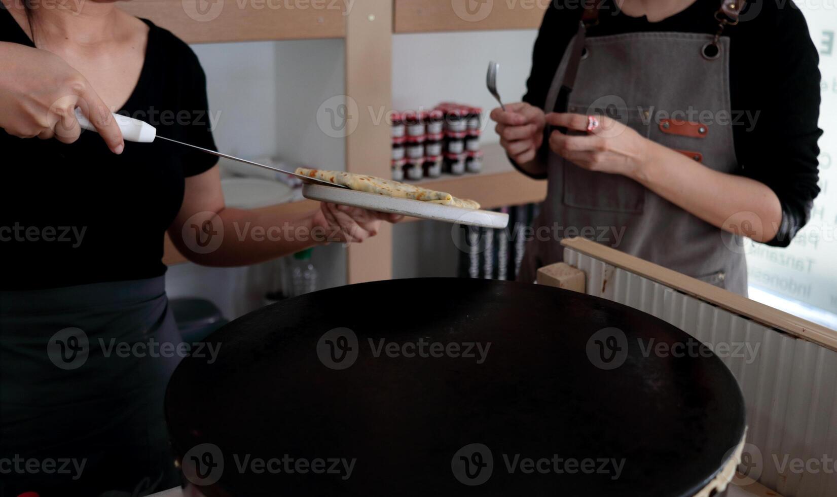 Woman in black cloth putting crepe on dish in left hand. photo