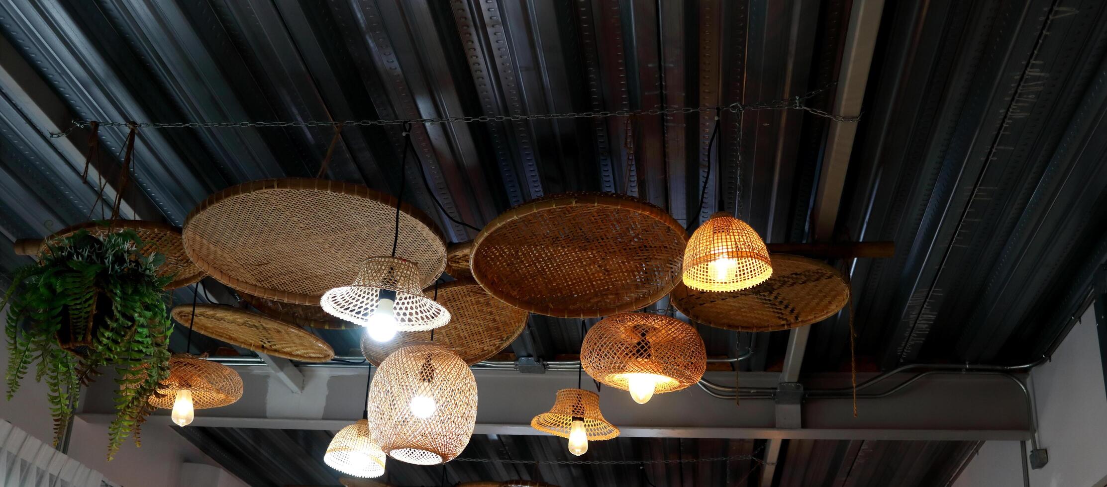 Group variety shape bamboo native Thai style weaving cover lamp hanging on dark gray wave shape metal ceiling in Thailand. photo