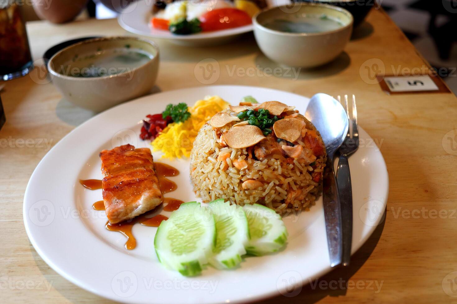 Salmon fried rice and salmon fellet streak on round white dish on wood table with garlic slice fried on top in Thailand. photo