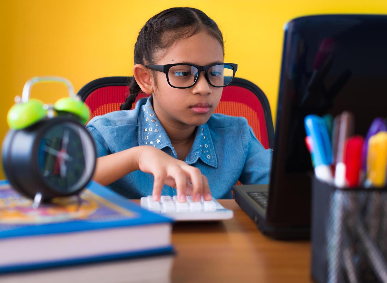 Cute girl wearing glasses using laptop and calculator on the desk isolated yellow background, Education concept. photo