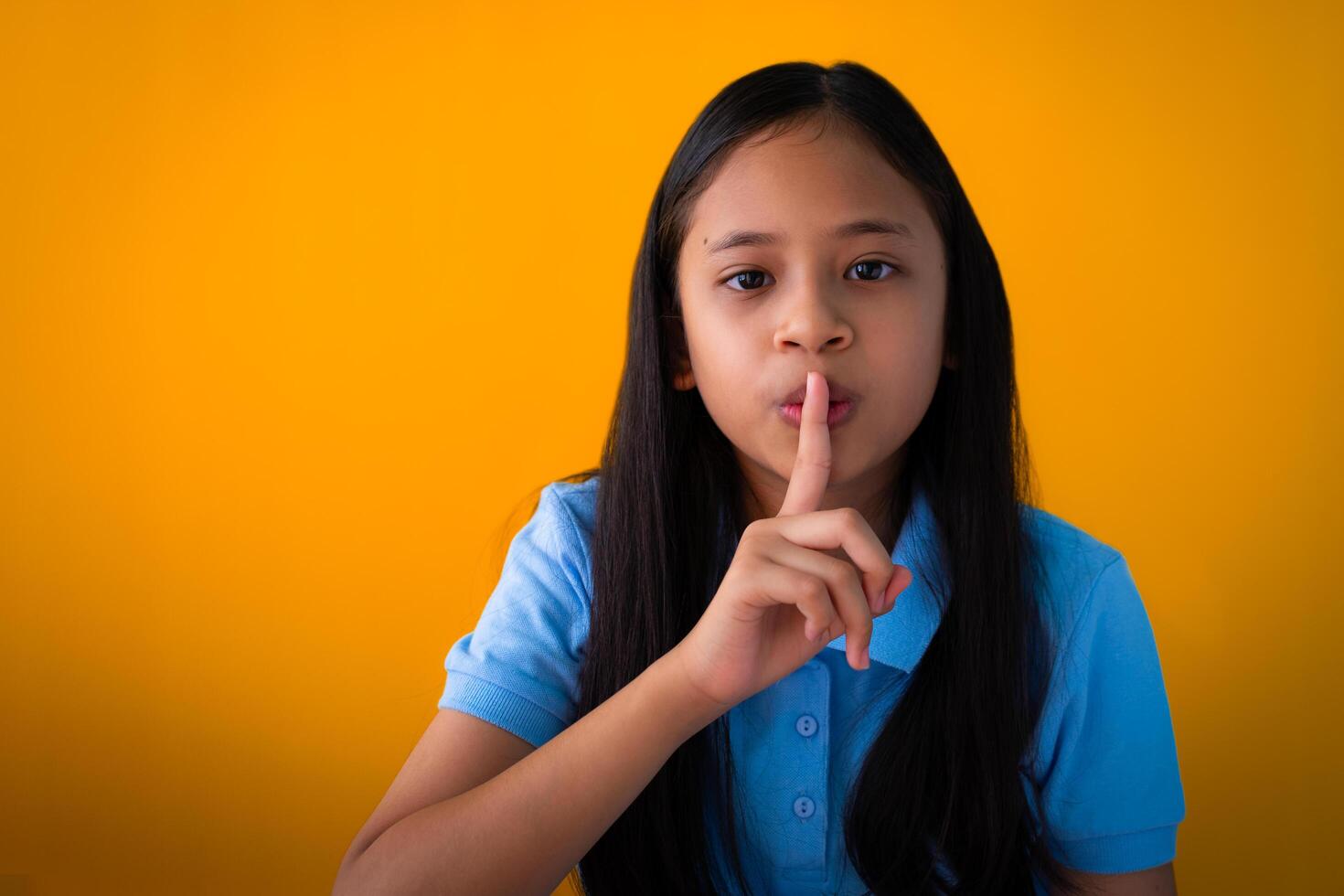 Indoor portrait of pretty asian girl with calm face expression. Photo of serious young girl with black long hair isolated on orange background.