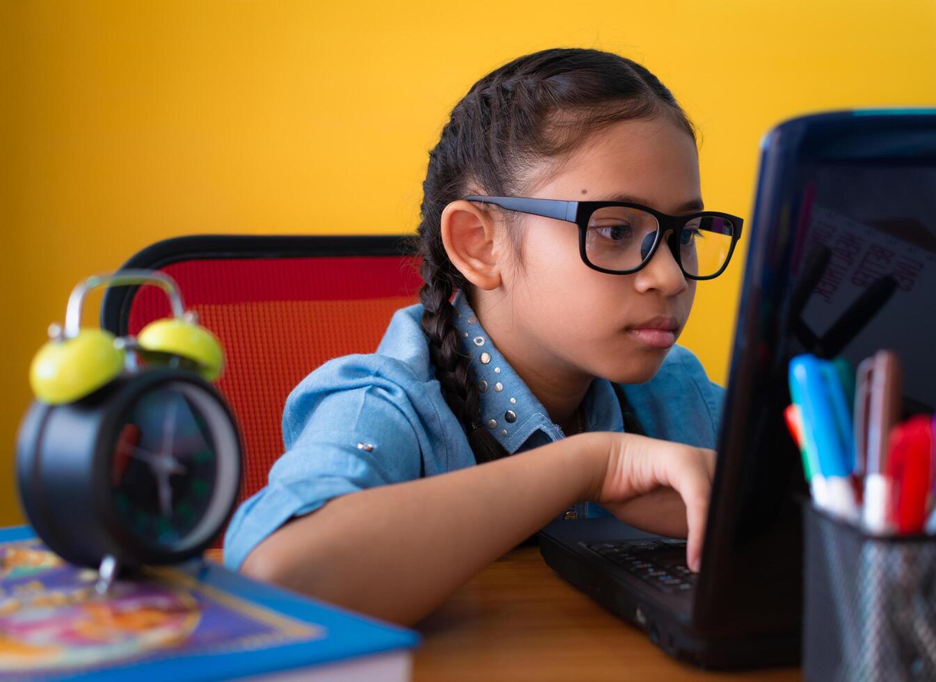 Cute girl wearing glasses using laptop on the desk isolated yellow background, Education concept. photo