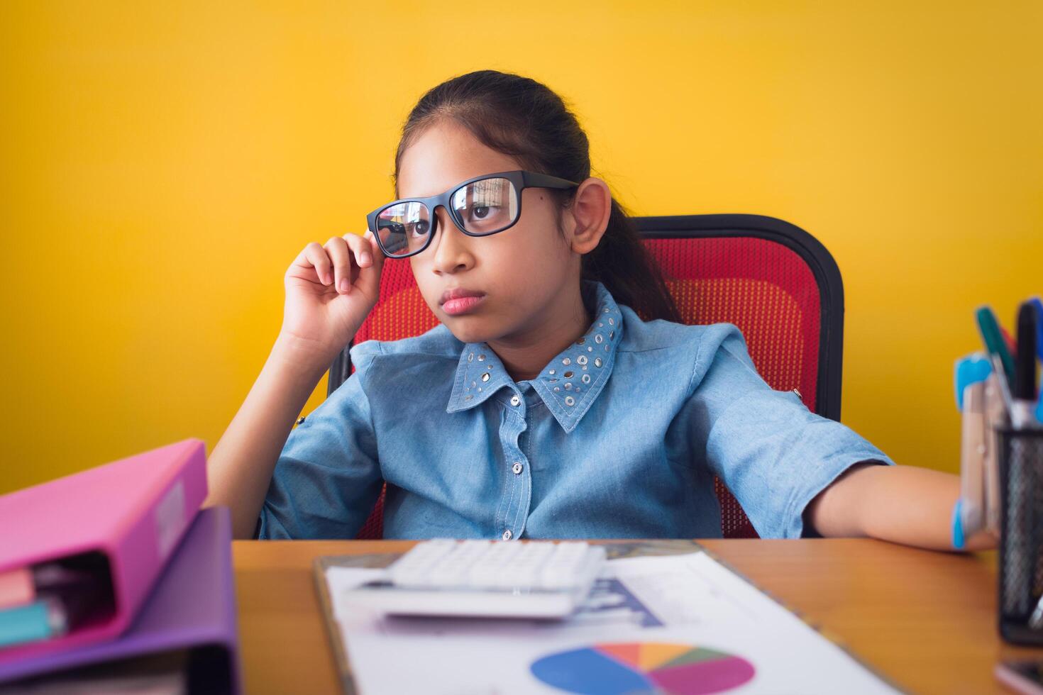 Cute girl wearing glasses using the idea of planning work on the desk with document isolated yellow background, Education concept. photo