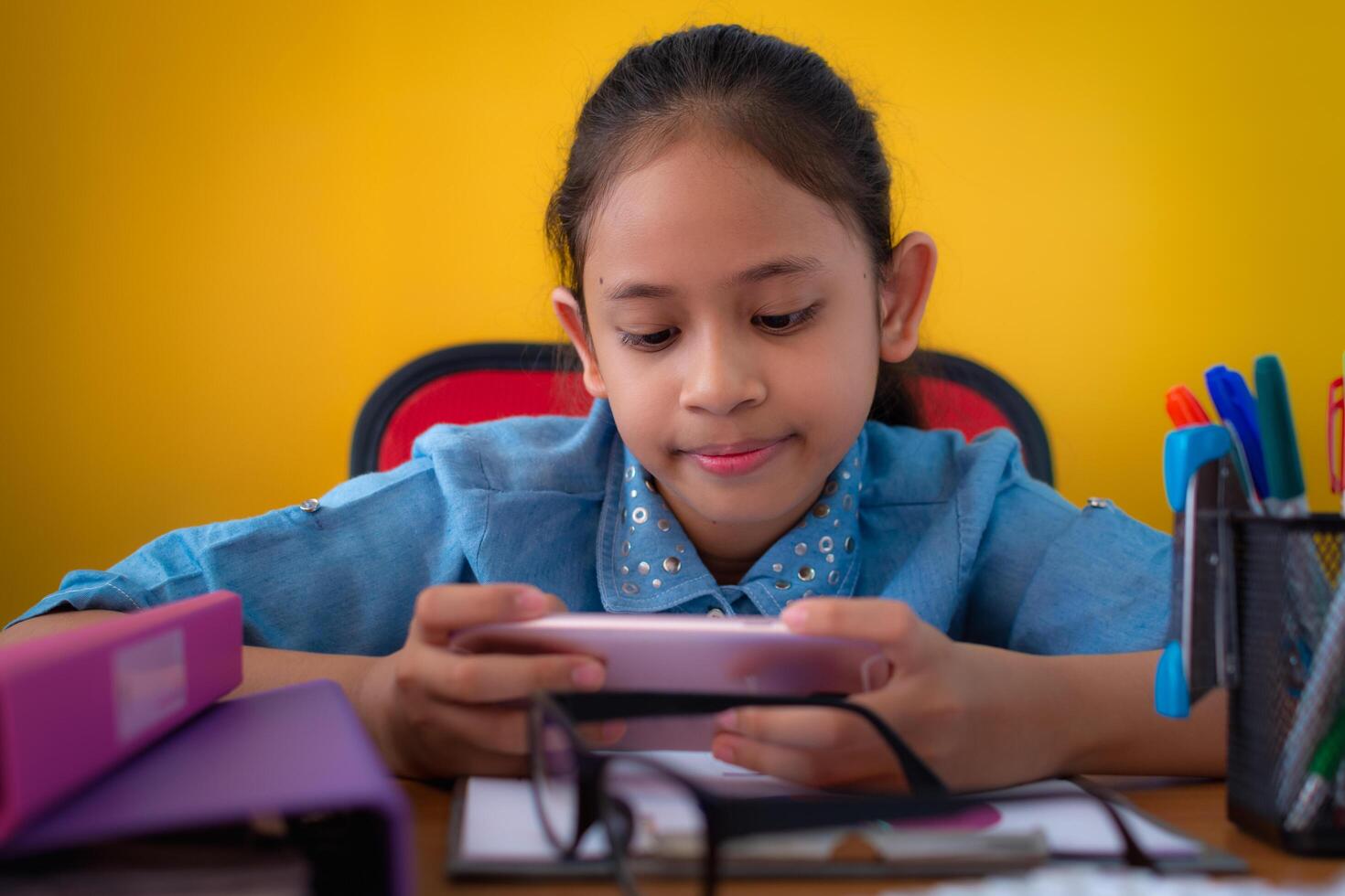 Cute girl smiling and using a mobile phone on working desk isolated yellow background, Education concept. photo