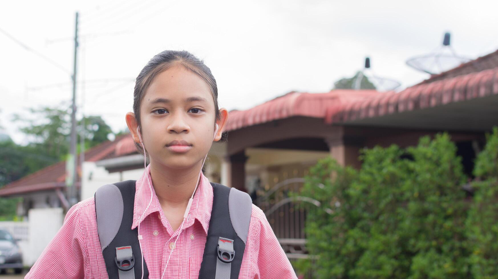 Portrait Asian high school girl in uniform with backpack wears earphones posing and looking at camera. photo