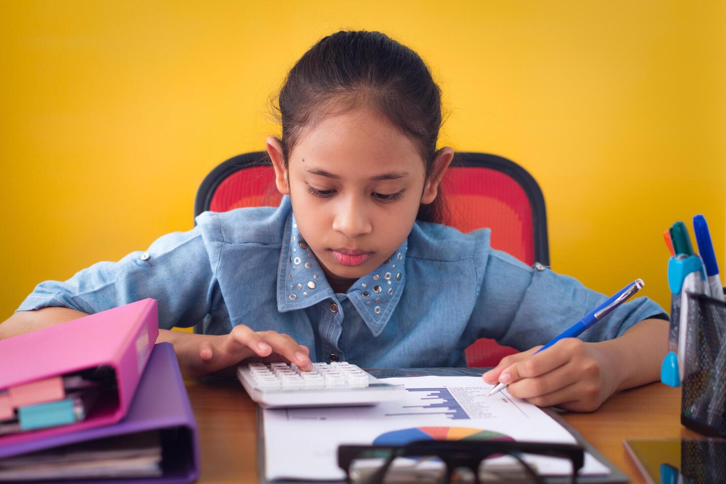 Cute girl working with calculator on the desk with document isolated yellow background. Education concept. photo