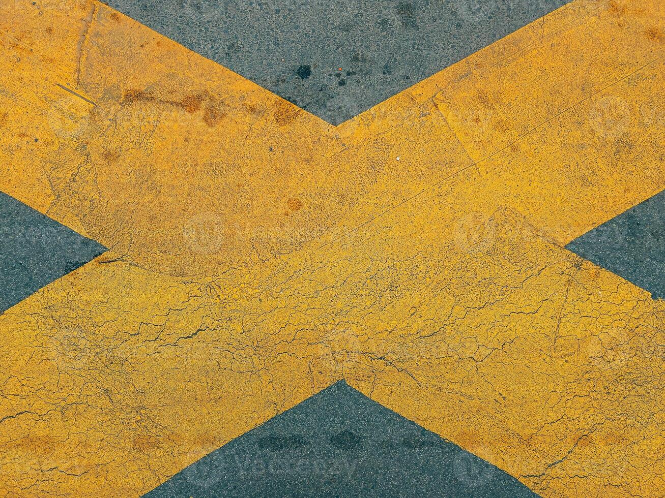 Yellow cross X marking on dark asphalt road surface photo