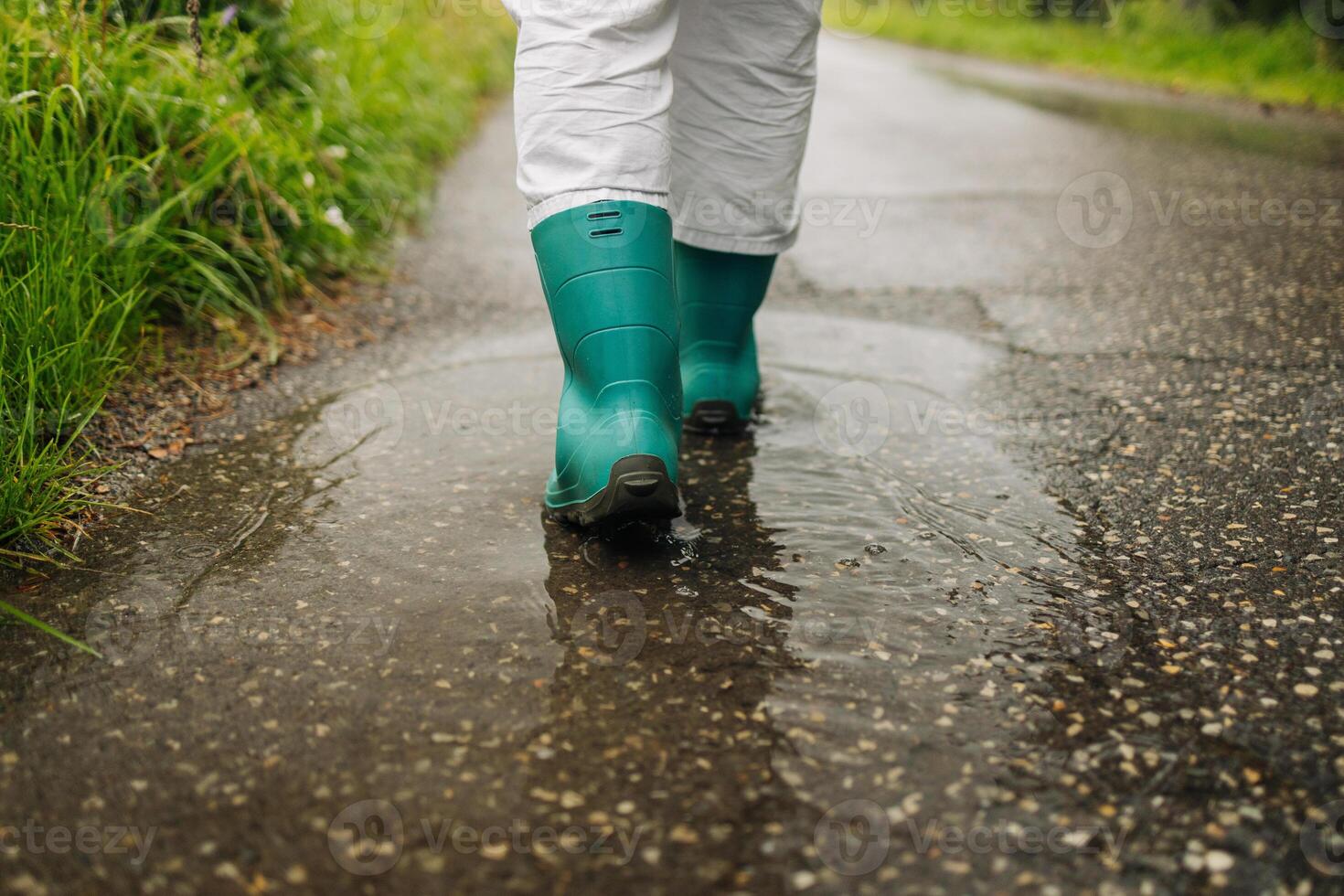 Woman wearing rain rubber boots walking running and jumping into puddle with water splash and drops in autumn rain. photo