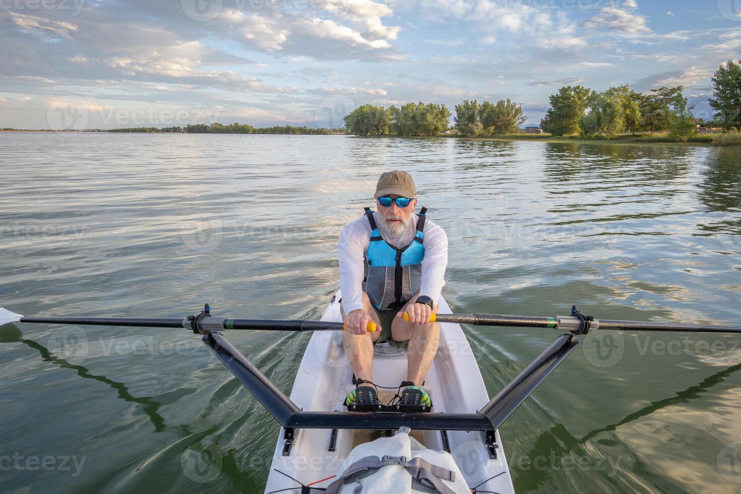 senior man in a rowing shell on a calm lake in Colorado in summer scenery photo