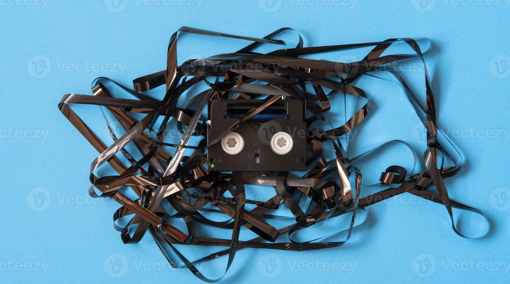 Old black mini DV cassette with tangled tape surrounding the cassette photo