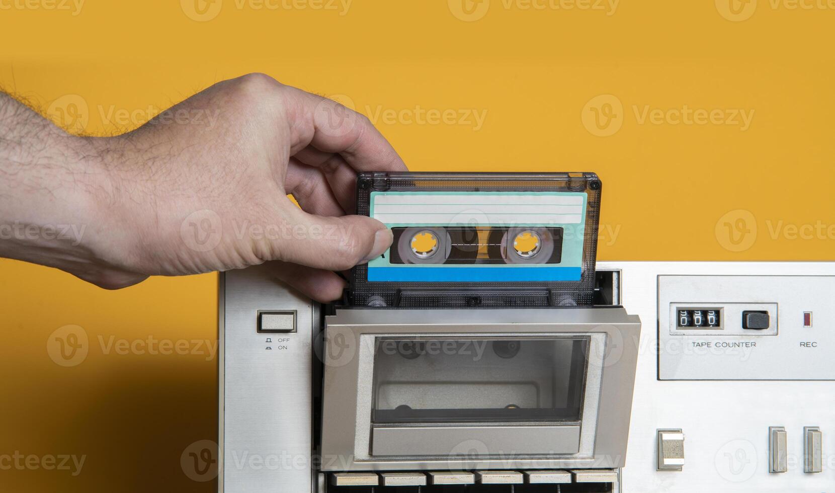man's hand inserting old music cassette into aluminum recorder against yellow background photo